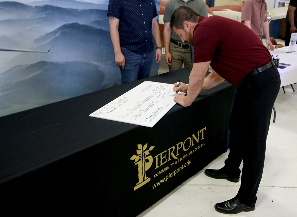 Michael Genin, Director of Operations at MHIRJ, signs the prop check at the Aviation Career Fair during the check signing event.